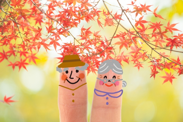 紅葉の下で並んで立つ老夫婦